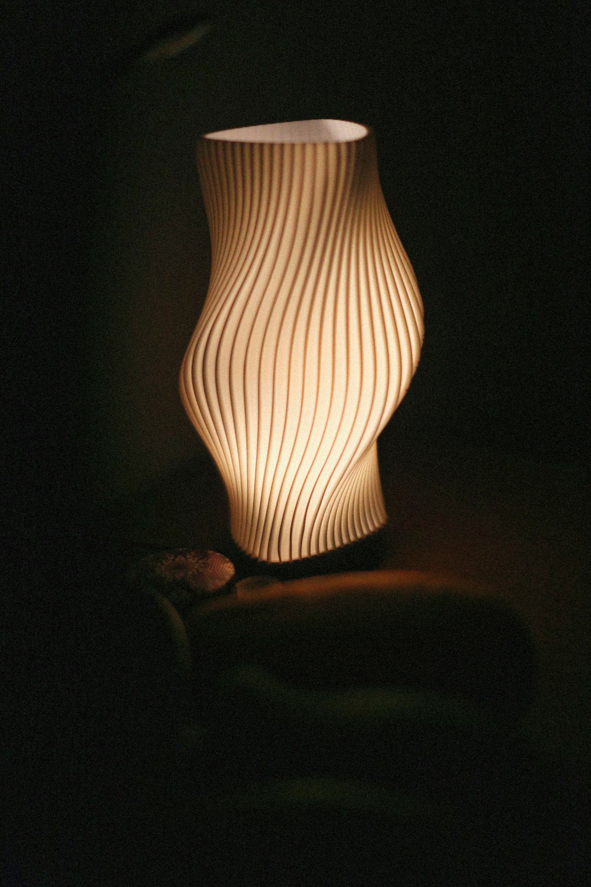 A ribbed 3D-printed lamp glowing with warm light in a dark room